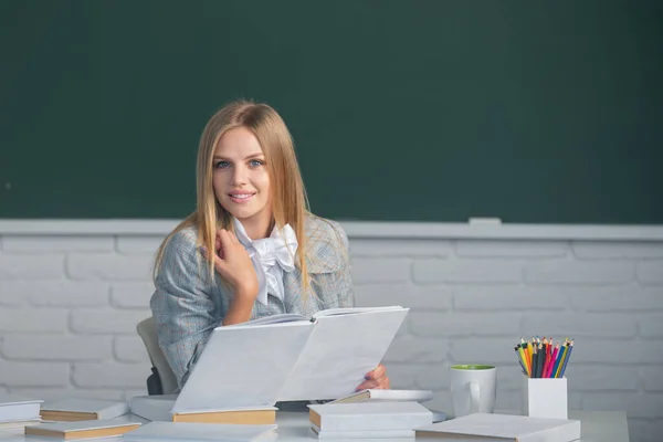 Portret van jonge vrouwelijke college student lezen boek, studeren in de klas op de klas met schoolbord achtergrond. — Stockfoto