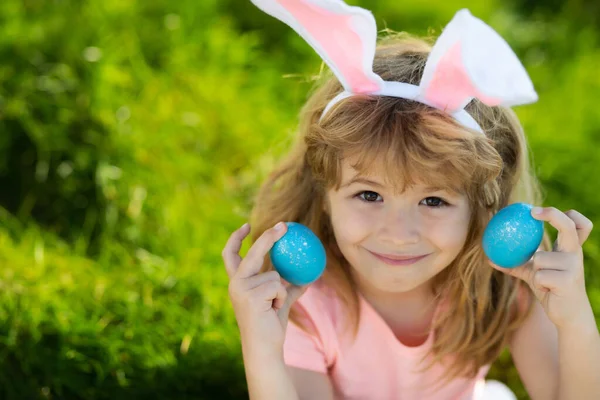 Criança da Páscoa de coelho. Crianças a caçar ovos de Páscoa. Rapaz com ovos de Páscoa e orelhas de coelho no quintal. Férias de primavera. — Fotografia de Stock