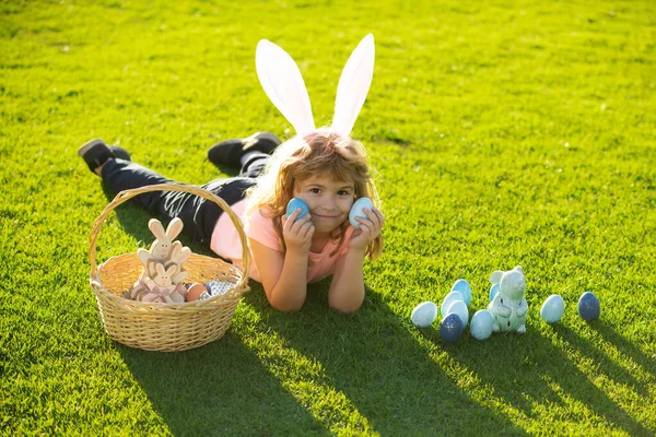 Chłopiec w stroju królika z króliczymi uszami polujący na wielkanocne jaja na trawie w parku wiosennym. Wesołych Świąt. — Zdjęcie stockowe