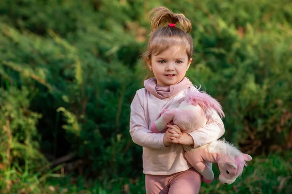 Söt liten flicka med leksak på grönt gräs på sommaren. Rolig liten grabb på naturen. Lycklig barndom. — Stockfoto