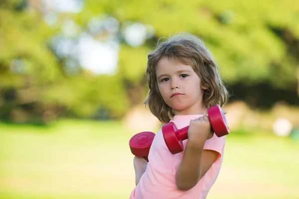 Güçlü pazı kasları olan sporcu çocuk. Spor yapan çocukların halterleri. Güçlü küçük çocuk parkta dambılla egzersiz yapıyor. Spor portresi çocuklar.. — Stok fotoğraf