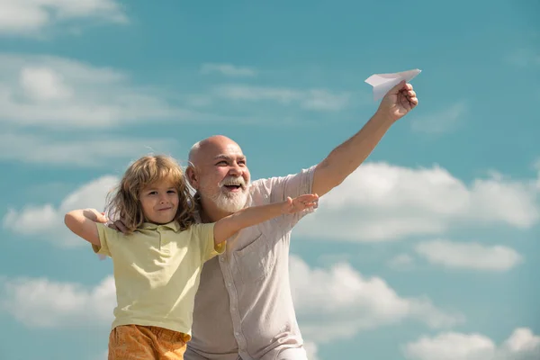 Avô e neto brincando com avião de papel contra fundo céu de verão. Menino com sonhos de voar ou viajar. — Fotografia de Stock