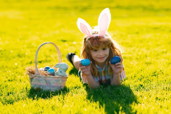 Kinderen in konijnenoren op paaseieren jacht in de tuin. Kinderen met kleurrijke eieren in gras. Peuter jongen spelen buiten. Op paaseieren jagen. — Stockfoto