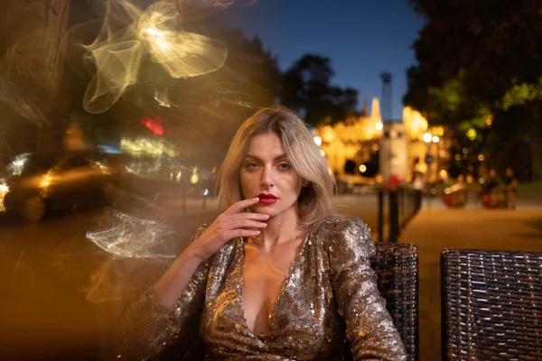 Foto de estilo callejero de la elegante mujer de moda con ropa de moda relajarse en la cafetería de la noche. Modelo en calle de ciudad europea. —  Fotos de Stock