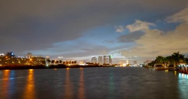 Miami Panorama zaman aşımı. Miami plaj şehrinde gece gökyüzü zamanı. Şehir manzarasında gün batımının hızlanması ve su dalgalanması yansıması ile hareket eden bulutlar.