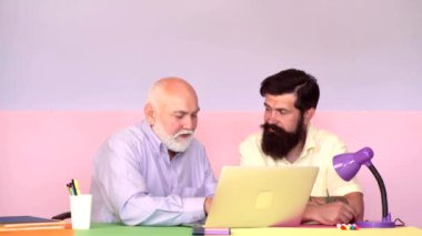 Yetişkin oğul, yaşlı babaya bilgisayarda yardım ediyor. Bilgisayarı kullanan adamlar ekranda çalışırken ofis masasında, profesyonel çalışanlar iş yerinde dizüstü bilgisayarda e-posta yazarken..