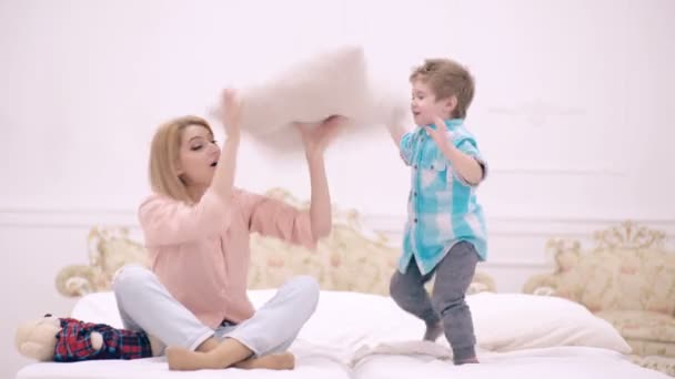 Mamma och sonen leker med kudden i sovrummet. Mor med liten son leker i sängen på helgen tillsammans, lat morgon. — Stockvideo