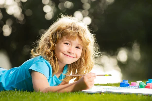 Carino il piccolo artista. Il bambino disegna in parco posa in erba divertendosi su sfondo naturale. Bambini concetto di educazione creativa. — Foto Stock