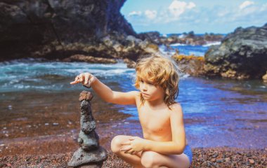 Şirin çocuk deniz kıyısında taş yığıyor doğada. Okyanus sahilindeki Cairn, beş çakıl kulesi. Denge ve uyum kavramı. Sakin ve ruhlu.