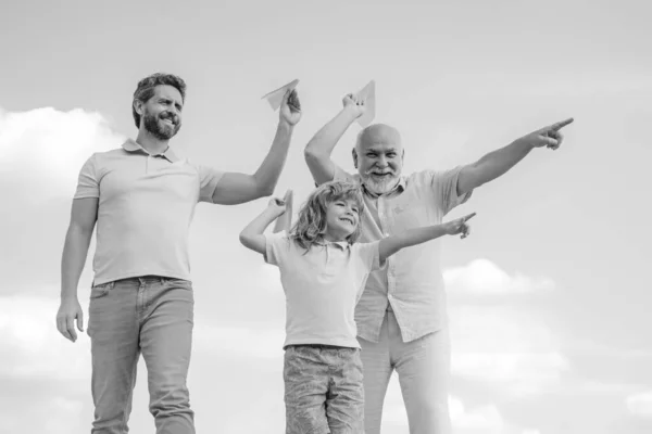 Großvater Vater und Sohn spielen draußen am Himmel mit Papierfliegern. Glückliche Familie. Drei Männer. Glückliche Kindheit. — Stockfoto