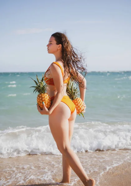 Sexy woman holding fresh pineapple. Buttocks of girl in bikini with fruit pineapple on beach background, summer vacation, healthy food and fitness. — Stock Photo, Image