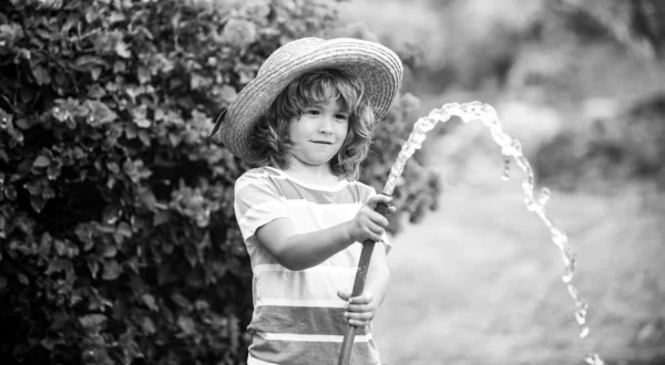 Смішний маленький хлопчик грає з садовим шлангом на задньому дворі. Дитина розважається з розпиленням води на фоні природи двору. Літні діти на відкритому повітрі . — стокове фото
