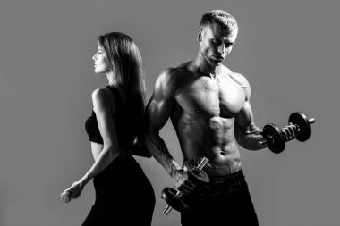 Kaslı seksi çift vücudu. Sporcular dambıllarla çalışıyor. Fit çift karanlık stüdyoda dambıllarla egzersiz yapıyor..