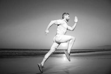 Doğada koşan atletik genç adam. Fit adam fitness modeli deniz kıyısında çalışıyor. Dinamik çalışma hareketi.