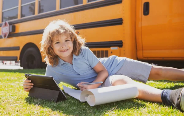 Porträt eines kleinen Schülers, der draußen im Schulpark schreibt und Hausaufgaben macht. — Stockfoto