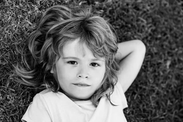 Słodki chłopak leżący w trawie. Przystojne dziecko cieszące się na polu lub trawniku i marzy. — Zdjęcie stockowe