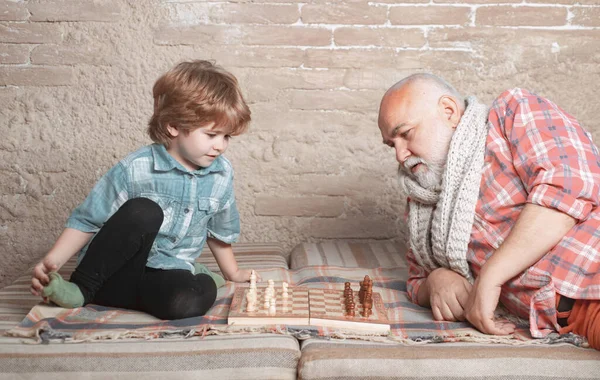 Petit garçon jouant aux échecs avec son grand-père. Pièce d'échecs. Senior homme penser à son prochain mouvement dans un jeu d'échecs. — Photo