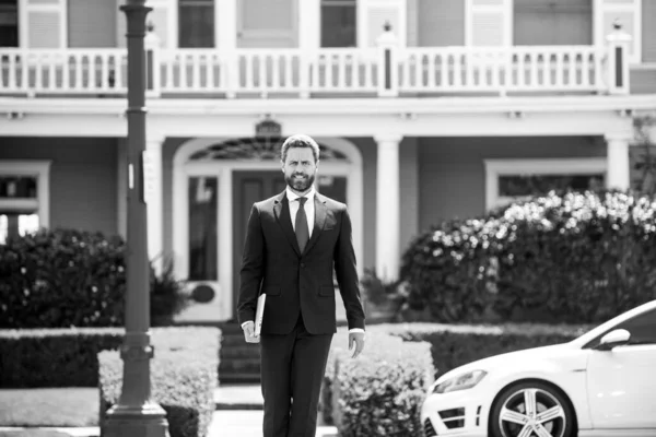 Ακίνητα. Πράκτορας έτοιμος να πουλήσει το σπίτι του. Επιχειρηματίας στέκεται έξω από ένα σύγχρονο σπίτι. — Φωτογραφία Αρχείου