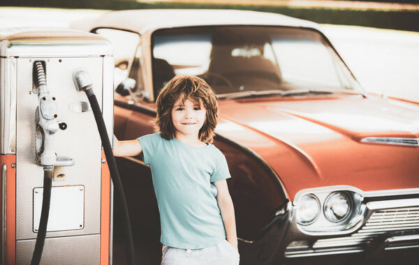 Retro gas station. Smiling Kid boy at the gas station. Waiting for fuel. Kid fueling vintage car at gas station. Refuel fill up with petrol gasoline.