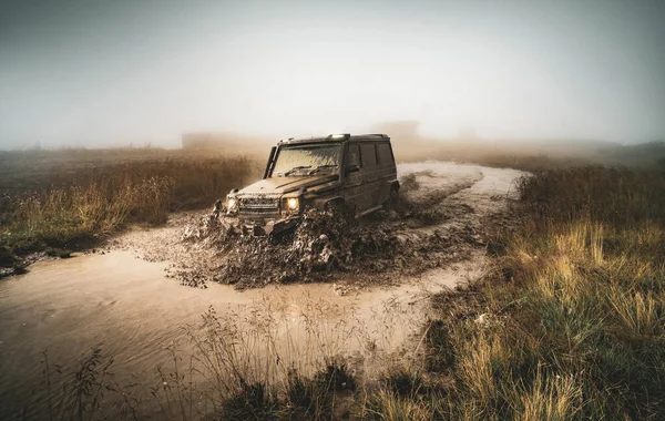 Rueda de cerca en un paisaje rural con un camino fangoso. Vehículo todoterreno atrapado en una carretera impenetrable después de la lluvia en el campo . — Foto de Stock