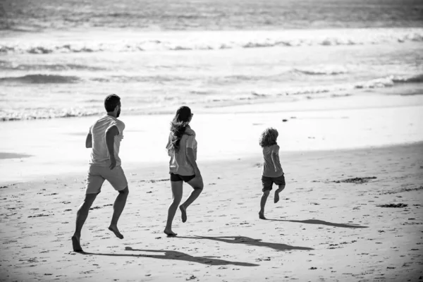 Feliz joven familia correr y saltar en la playa de verano. Niño con padres corriendo y saltando. Viajes en familia, concepto de vacaciones. —  Fotos de Stock