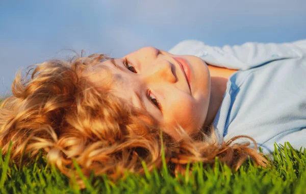 Portret van een lachend jongetje liggend op groen gras en dromend. Schattig kind genietend van de natuur buiten. Gezond zorgeloos kind spelen buiten in het zomerpark op een grasveld. — Stockfoto