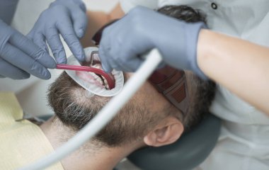 Genç adam, diş hekimi, diş rengini seçme yakın çekim. Kadın dişçi ile modern diş Kliniği aynada hasta diş kontrol. Yakışıklı dişçi ofisinde.