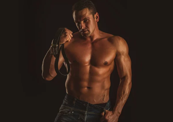 Сексуальна людина з м'язовим тілом і голий торс. Чоловік тримає шкіряний пояс . — стокове фото