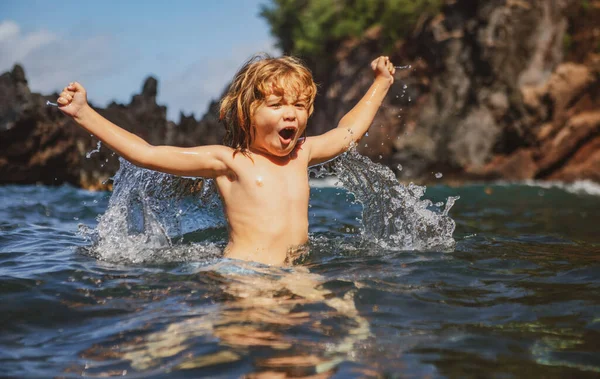 Incroyable enfant jouant et éclaboussant dans la mer. Le gamin s'amuse dehors. Vacances d'été et mode de vie sain en famille concept. Petit garçon lève les mains dans l'eau et éclabousse gouttes d'eau. — Photo