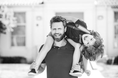 Baba, okul sonrası oğlunu sırtında taşıyor. Sırt çantalı ilkokul öğrencisinin ebeveyni ve öğrencisi..