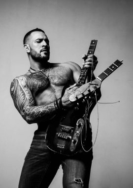 Müzik dükkanı. Yetişkinler için öğrenme ve çalma müziği. Müzik ve DJ konsepti. Sakallı, stil sahibi, vahşi bir adam, bir dövme gitarda bir oyunu taklit ediyor. Tıraşsız, konsantre bir adam. Bir erkeğin seksi görünüşü.