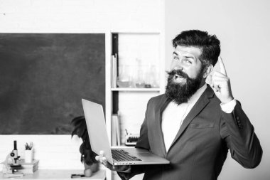 Okuldaki sınıfta dizüstü bilgisayarını gösteren heyecanlı bir öğretmen. Öğrencileri bekleyen hayret verici öğretmen, özgüvenle gülümsüyor. Pozitif ifade duyguları komik yüz.
