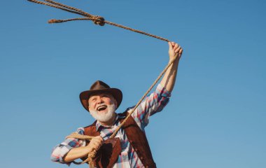 Kementle asılmış vahşi batı kovboyu. Kahverengi ceketli, şapkalı, at ya da inek yakalayan sakallı batılı adam..