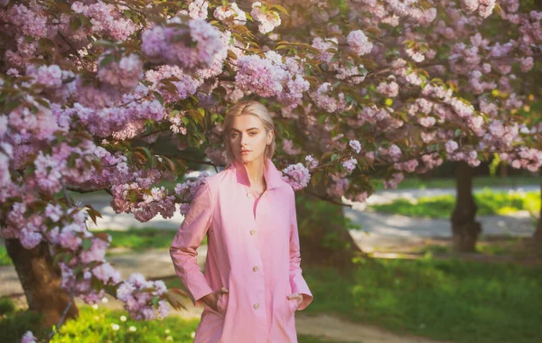 春のファッション、ピンクのコートの女の子は庭で桜をお楽しみください。花は女性を幸せにします。春の花。優しさと女性らしさ。桜. — ストック写真