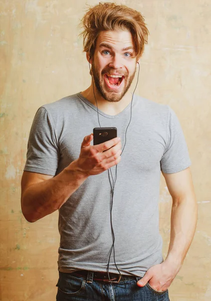 Mies innoissaan älypuhelimen kuuntelee musiikkia. Yllättynyt mies puhelimen ja kuulokkeiden kanssa. Tunteellinen muotokuva homo kaveri. — kuvapankkivalokuva