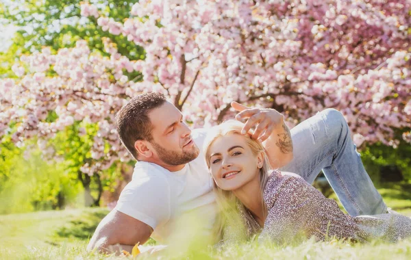 Ευτυχισμένο ανοιξιάτικο ζευγάρι ερωτευμένο που διασκεδάζει. Δύο νέοι που χαλαρώνουν με λουλούδια σακούρα. Χαμογελαστοί εραστές χαλαρώνουν στο πάρκο. Η οικογένεια πάνω από τη φύση ανθίζει φόντο. Σχέσεις και χρονολόγηση. — Φωτογραφία Αρχείου