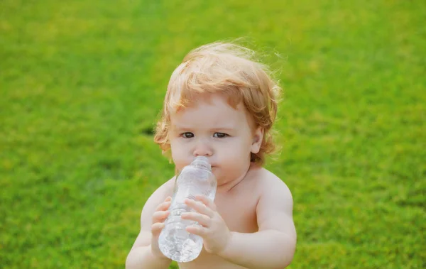 Детская питьевая вода. Крупный план ребенка, пьющего свежую и чистую воду из бутылки на размытом зеленом фоне травы. — стоковое фото