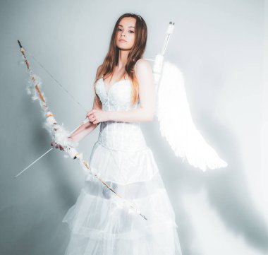 Oklu ve yaylı sevimli kız aşkını bulmaya hazır. Mutlu genç melek kız. Sevgililer Günü 'nü kutlayan ok ve yaylı aşk tanrısı kadar güzel beyaz bir kız..