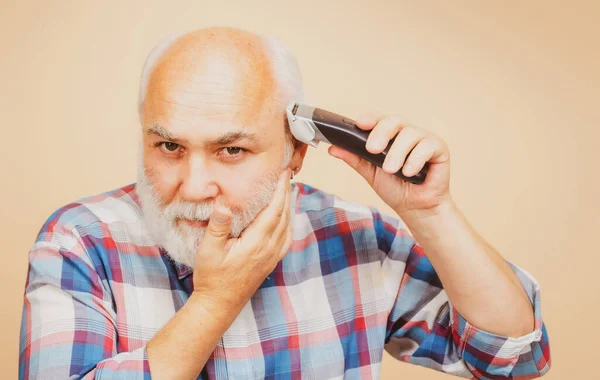 理髪店でヘアクリッパーでトリミングされている老人の肖像画、電動カミソリでヘアカット。男性の髪の治療. — ストック写真