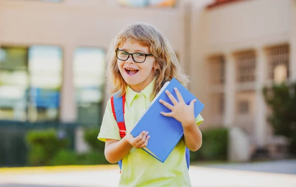 Niño alegre con gran mochila divirtiéndose contra la escuela. Regreso al concepto escolar. —  Fotos de Stock