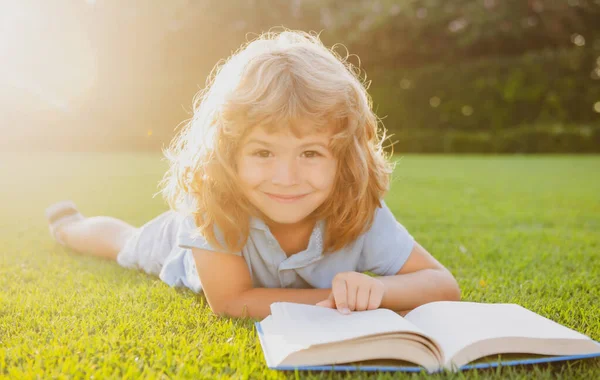 Een jongen die een interesseboek leest in de tuin. Zomertijd leuk. Leuke jongen liggend op het gras het lezen van een kids boek. — Stockfoto