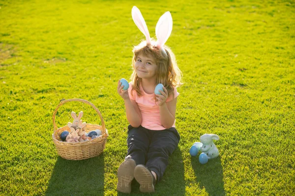 Pasen kinderen jongen in konijnenoren jagen paaseieren buiten. Schattig kind in konijnenkostuum met konijnenoren die plezier hebben in het park. Grappige jongen, paashaas kinderen. — Stockfoto