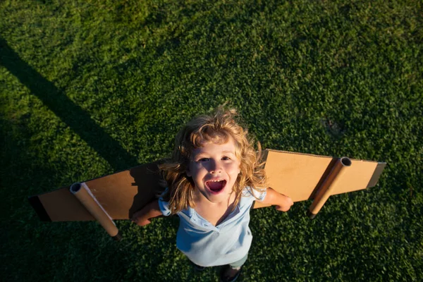 Rapaz rindo, menino sonhador bonito brincando com um avião de papelão. Infância. Fantasia, imaginação. Criança sorridente sonhando com férias de verão e viagens. — Fotografia de Stock