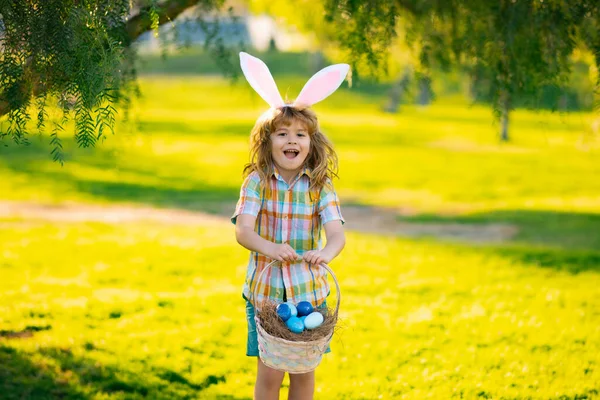 Konijnenjongen. Een jongetje dat op paaseieren jaagt en op gras legt. Kind in konijnenoren buiten. Paashaas kinderen. — Stockfoto