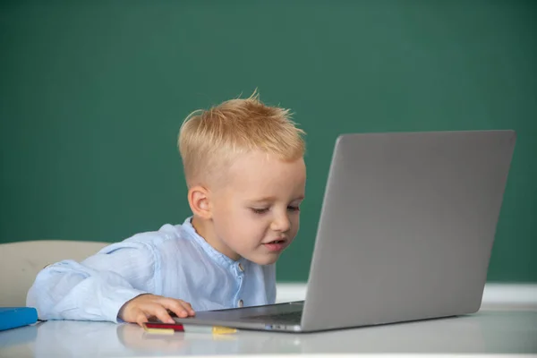 Menino da escola aprender lição sentado na mesa, estudando on-line e-learning usar internet. Aluno loira engraçada no quadro negro. — Fotografia de Stock