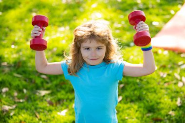 Yeşil parkta dambıllarla egzersiz yapan sevimli küçük çocuk. Dambılı spor çocuk portresi. Mutlu çocuk dışarıda egzersiz yapıyor. Sağlıklı aktiviteler, çocuk yaşam tarzı.