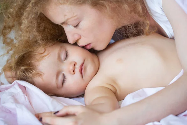 Mutter und Baby schlafen im Bett. Mutter küsst schläfriges Kind. Kindheits- und Familienkonzept, Innenporträt aus nächster Nähe. — Stockfoto