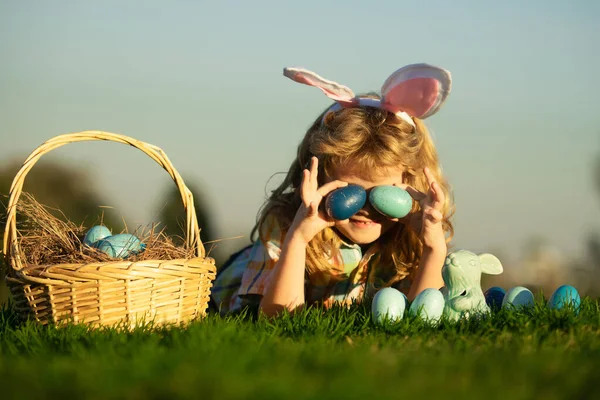 Охота на пасхальные яйца в саду. Дети играют в поле, охотятся на пасхальные яйца. Симпатичный кролик с кроличьими ушами, на фоне неба с копировальным пространством. — стоковое фото
