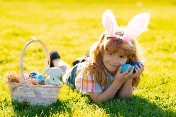 Kinderen in konijnenoren op paaseieren jacht in de tuin. Kinderen met kleurrijke eieren in gras. — Stockfoto