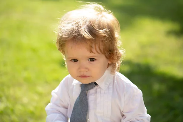Outdoor portrait of cute little boy in suit and necktie tie. Little businessman. Baby child in green grass on spring lawn. Little kids walking in the park. — Stock Photo, Image